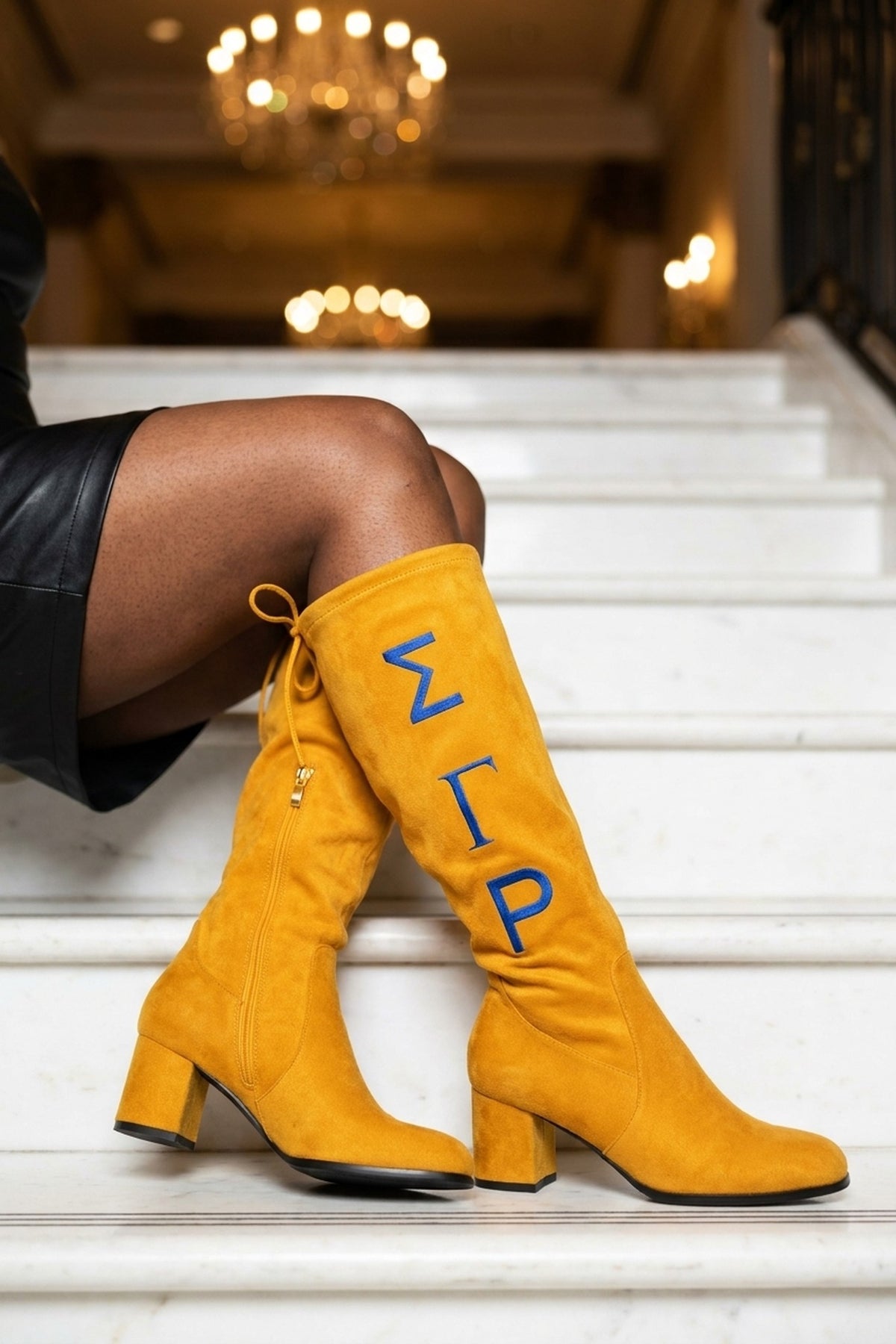 Sigma Gamma Rho Knee-High Boots in gold, seated on marble stairs